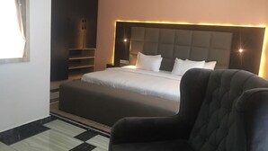 Een moderne hotelkamer met een groot bed, een donkere fauteuil en een inbouwkast voor de televisie.