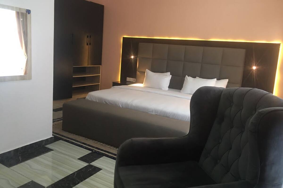 Ein modernes Hotelzimmer mit einem großen Bett, einem dunklen Sessel und einer integrierten TV-Konsole.