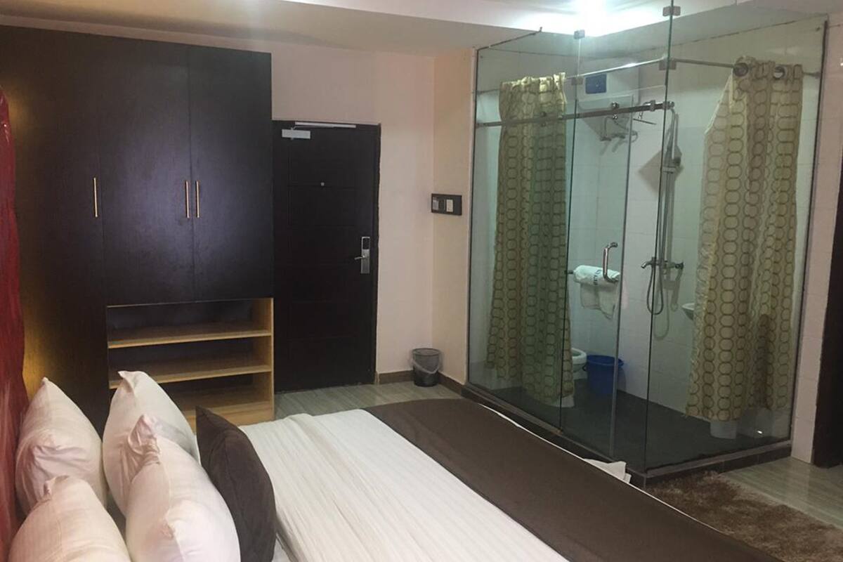 Ein Schlafzimmer mit Bett, Kleiderschrank, einer Duschkabine aus Glas und einer kleinen Mülltonne.
