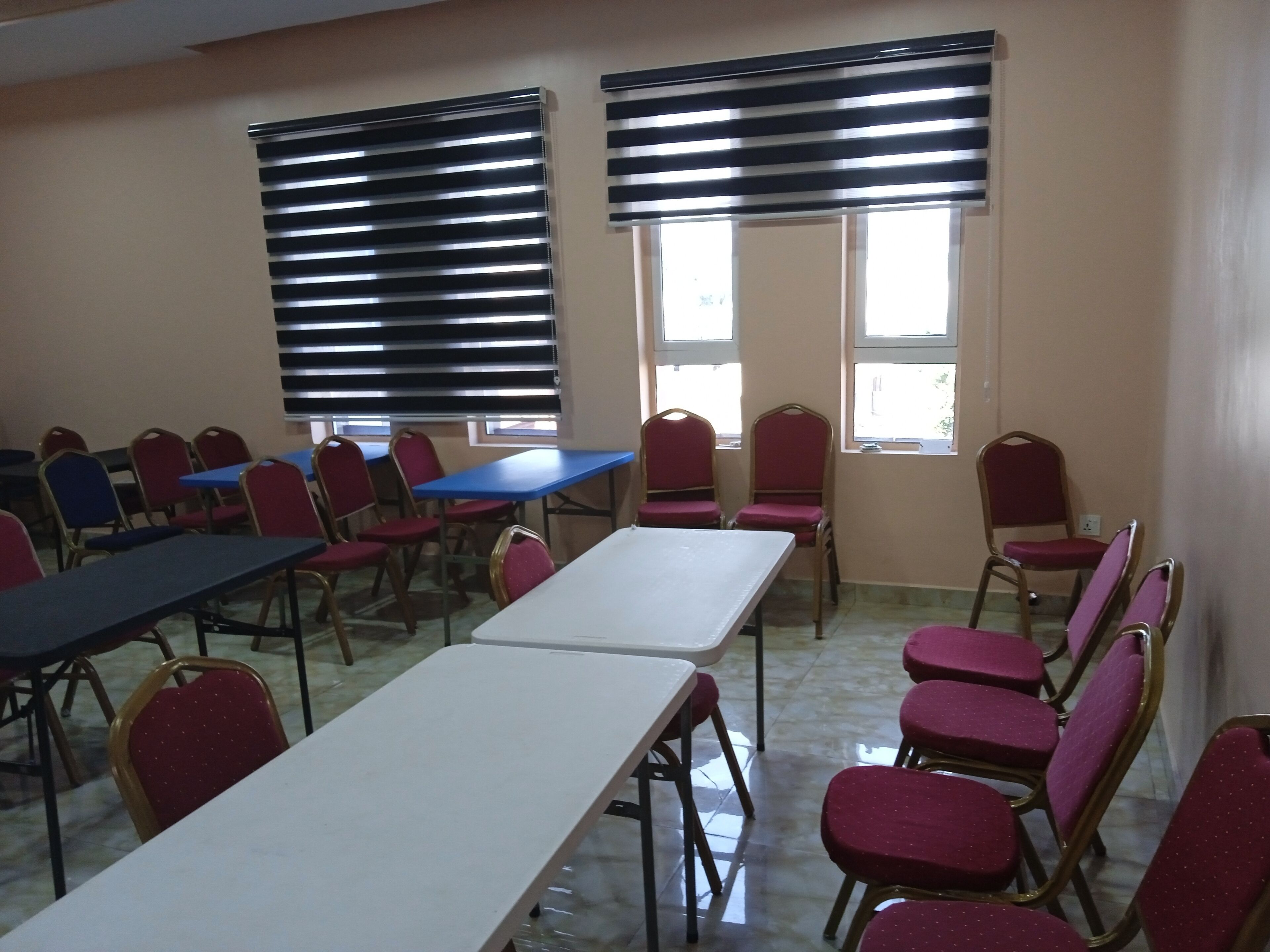 A conference room with tables and chairs, large windows with blinds, and a tiled floor.