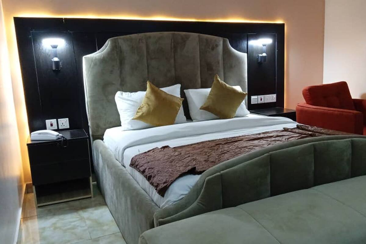 Ein Hotelzimmer mit einem großen Bett, einem Nachttisch, einem roten Sessel und einem hölzernen Kopfteil.
