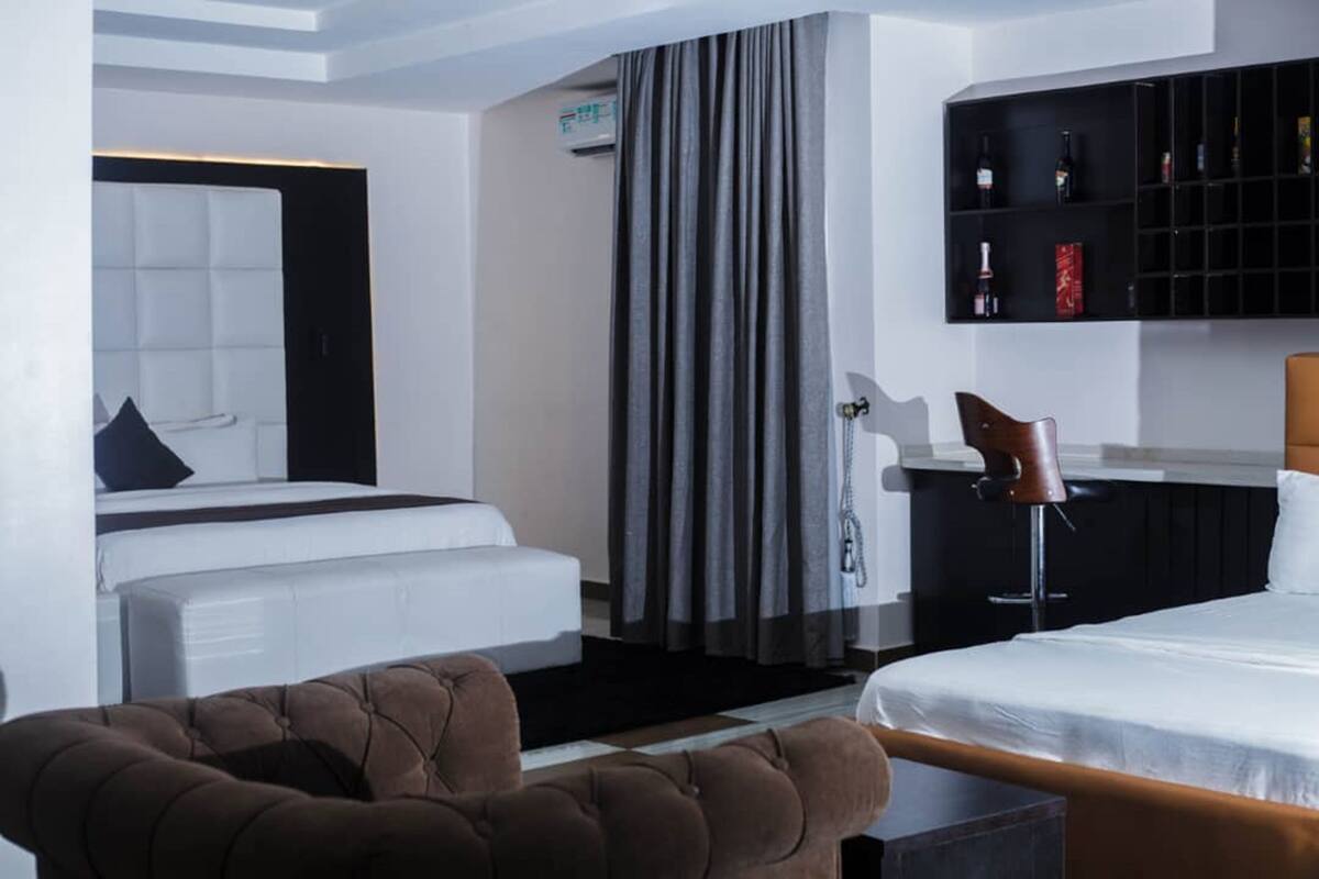 Ein modernes Hotelzimmer mit einem großen Bett, einer Sitzecke, einem Schminktisch mit Spiegel und einem Weinkühlschrank.