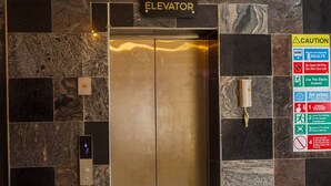 Een lift met een bordje dat aangeeft dat deze uitsluitend voor volwassenen is, een waarschuwing met instructies bij nood, en een digitaal scherm waarop het verdiepingsnummer wordt weergegeven.