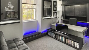 Een moderne woonkamer met een grijze bank, een televisie, een boekenkast en een raam met jaloezieën.