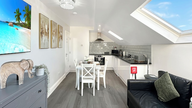 A modern apartment with a dining area, kitchen, and a living room with a black leather sofa and a skylight. - Granada Apartments Holmfield Rd flat 4 2nd floor loft type (Blackpool)