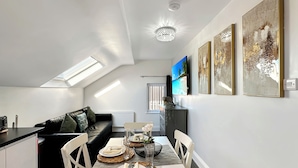 A modern dining area with a table set for two, a sofa, and a TV on the wall. - Granada Apartments Holmfield Rd flat 4 2nd floor loft type (Blackpool)