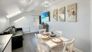 A modern living room with a dining area, featuring a high ceiling, skylight, and artwork on the walls. - Granada Apartments Holmfield Rd flat 4 2nd floor loft type (Blackpool)