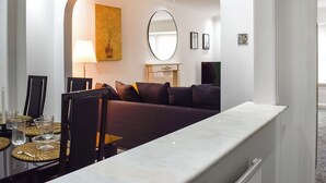 Moderni hotellihuone, jossa on ruokailutila, sohvaryhmä, pyöreä peili ja taulu seinällä.