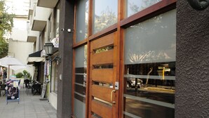 A storefront with a wooden door and large glass windows reflecting the street. - Living Pastene  (Santiago)