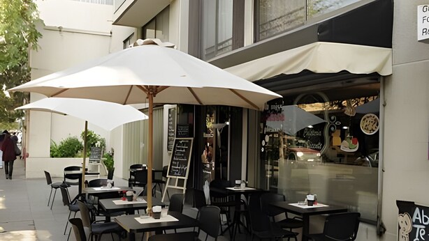 An outdoor cafe with tables and chairs under umbrellas, a chalkboard menu, and a view of the street. - Living Pastene  (Santiago)
