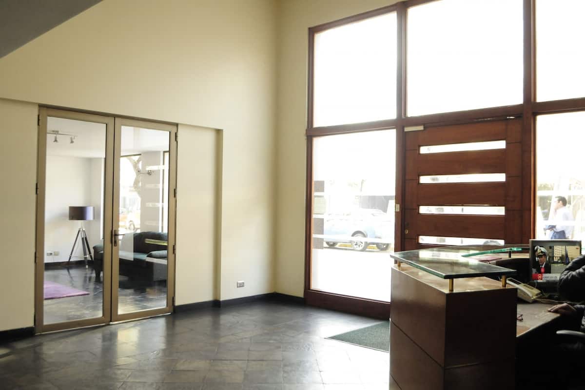 A reception area with a glass desk, a large window with a view of the street, and a sliding glass door leading to a room with a tripod lamp.