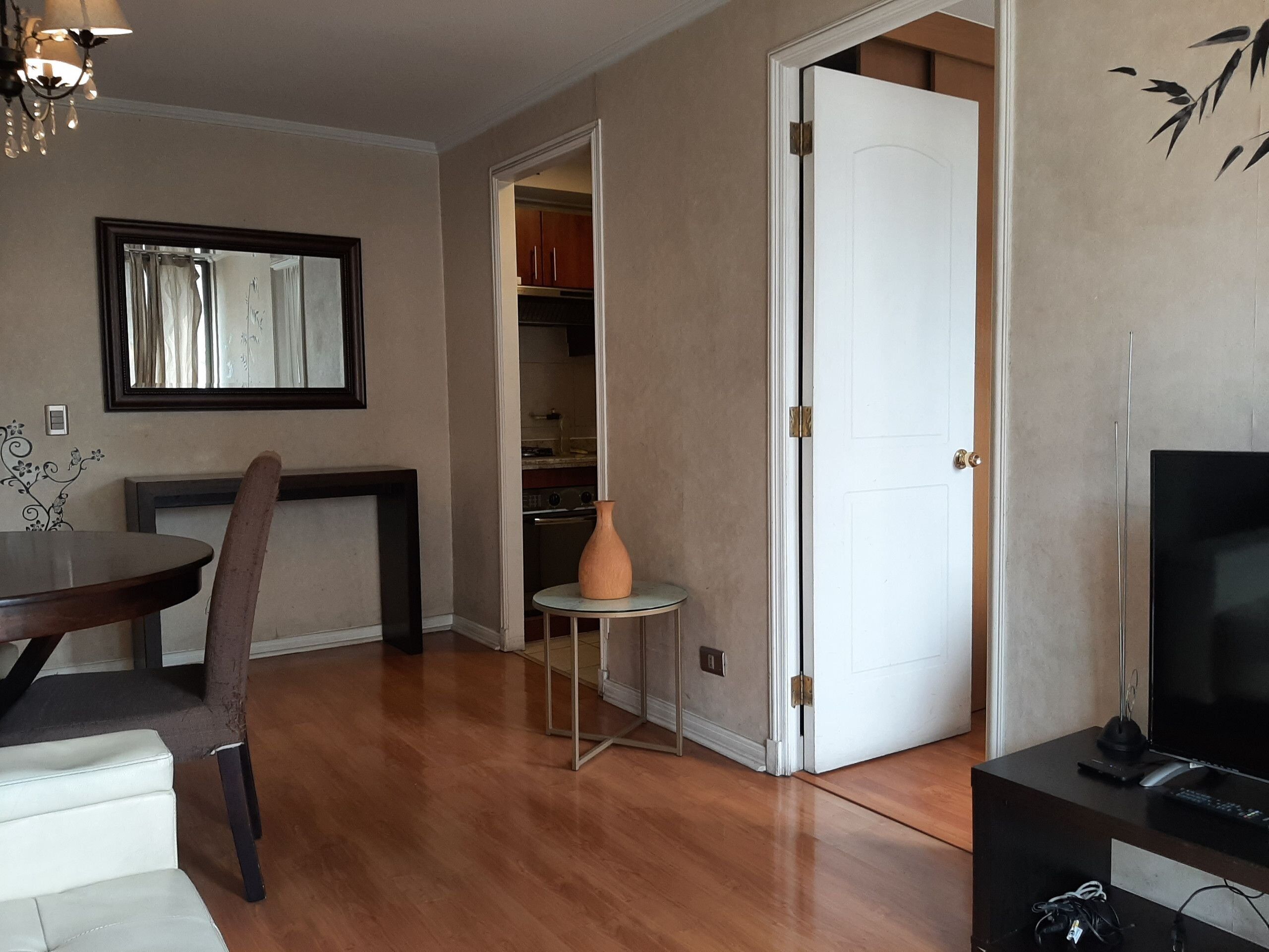 A dining area with a table and chairs, a vase on a side table, and a doorway leading to a kitchen.