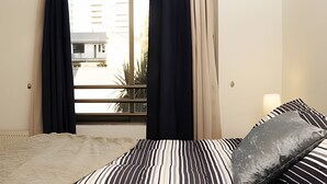 A hotel room with a bed, striped pillows, a window with curtains, and a view of buildings outside. - Living Pastene  (Santiago)