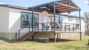 A single-story house with a covered porch, a staircase leading to the entrance, and a small outdoor seating area with chairs. - Peaceful Pastures near PK Lake (Graham)