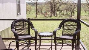 A balcony with wicker chairs and a small table, overlooking a grassy area with trees. - Peaceful Pastures near PK Lake (Graham)