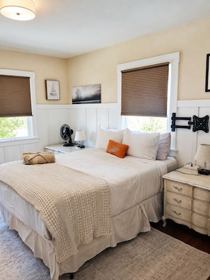 Une chambre à coucher avec un lit, des tables de chevet, une lampe, un ventilateur et des œuvres d’art accrochées au mur.
