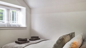 Un dormitorio con cama, almohadas, una ventana con persianas y una lámpara.