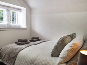 Un dormitorio con cama, almohadas, una ventana con persianas y una lámpara.