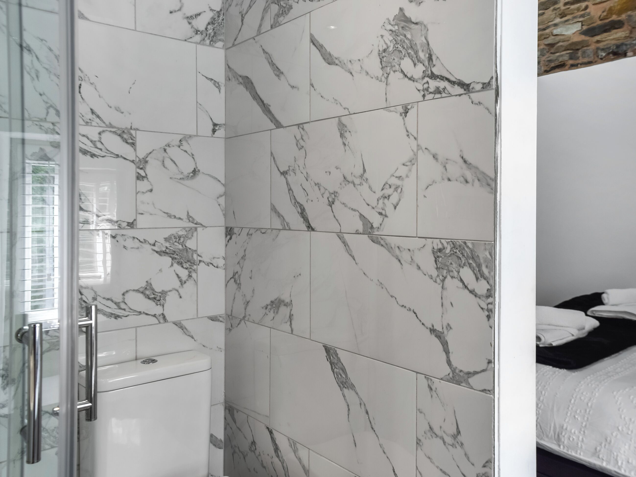 Une salle de bain carrelée de marbre, dotée d’une douche à parois de verre et de toilettes.