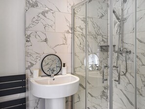 A bathroom with a marble-tiled wall, a white sink with a mirror, and a glass-enclosed shower area.