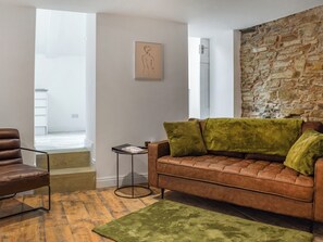 Una sala de estar con un sofá de cuero marrón, un tapete verde, una mesita auxiliar y una pared de piedra.