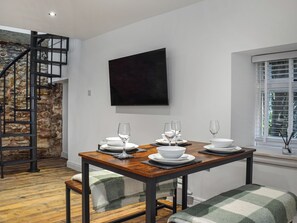 A dining area with a wooden table set for four, a stone wall, a staircase, and a window with blinds.