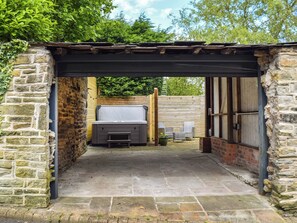 Une terrasse extérieure entourée de murs en pierre, dotée d’un jacuzzi, de fauteuils en osier et d’une pergola en bois.
