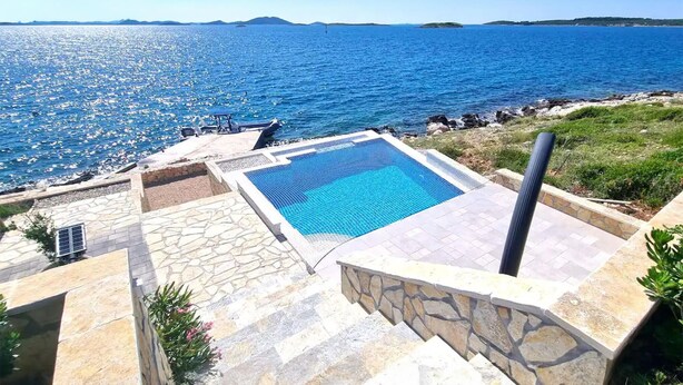 Ein Pool mit Meerblick, Steinstufen und einer Rasenfläche.