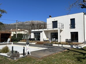 A modern two-story house with a balcony, large windows, and a paved patio area. - Villa Entre mer et Montagne (Saint-Vallier-de-Thiey)