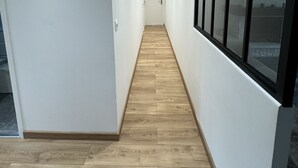 Un pasillo estrecho con suelo de madera y paredes blancas, que conduce a una puerta al final.