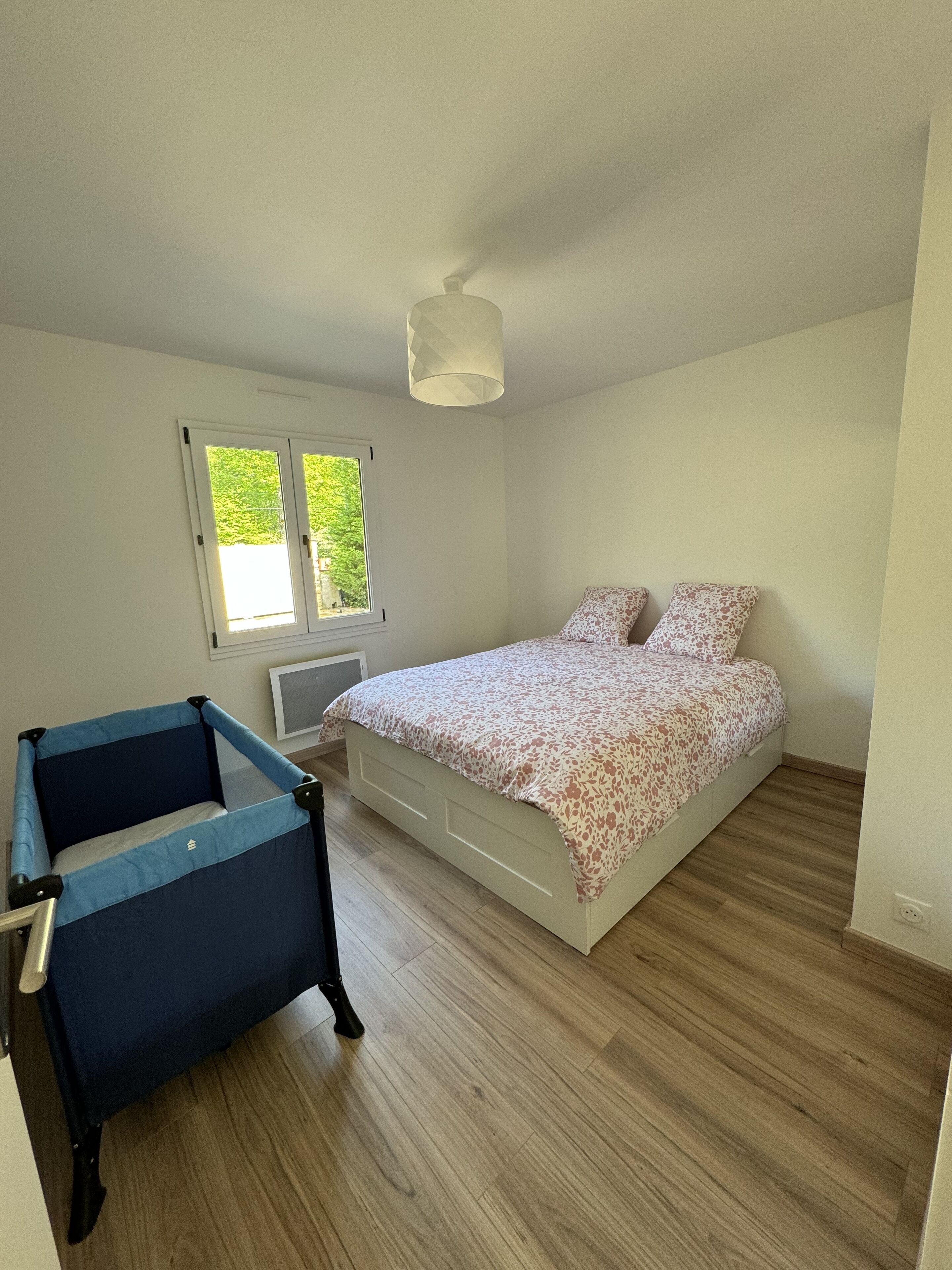 Un dormitorio con cama, una silla, un ventanal y una lámpara en el techo.