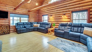 L'intérieur d'une cabane en rondins est aménagé avec un grand canapé d'angle, une table basse en bois et une grande fenêtre qui laisse entrer la lumière naturelle.