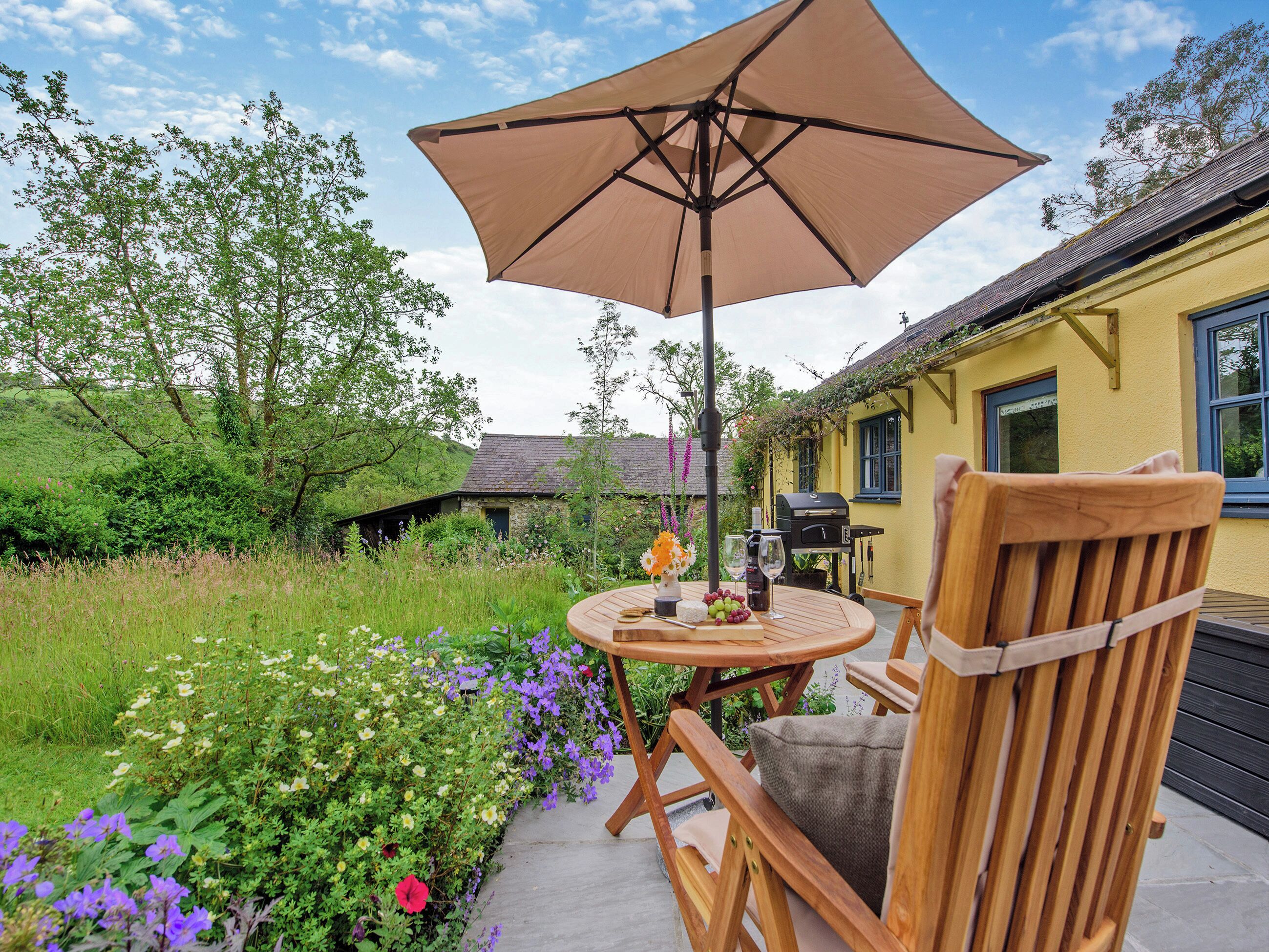 An outdoor patio with a wooden chair, a round table, and a large umbrella.