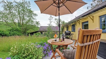 An outdoor patio with a wooden chair, a round table, and a large umbrella.