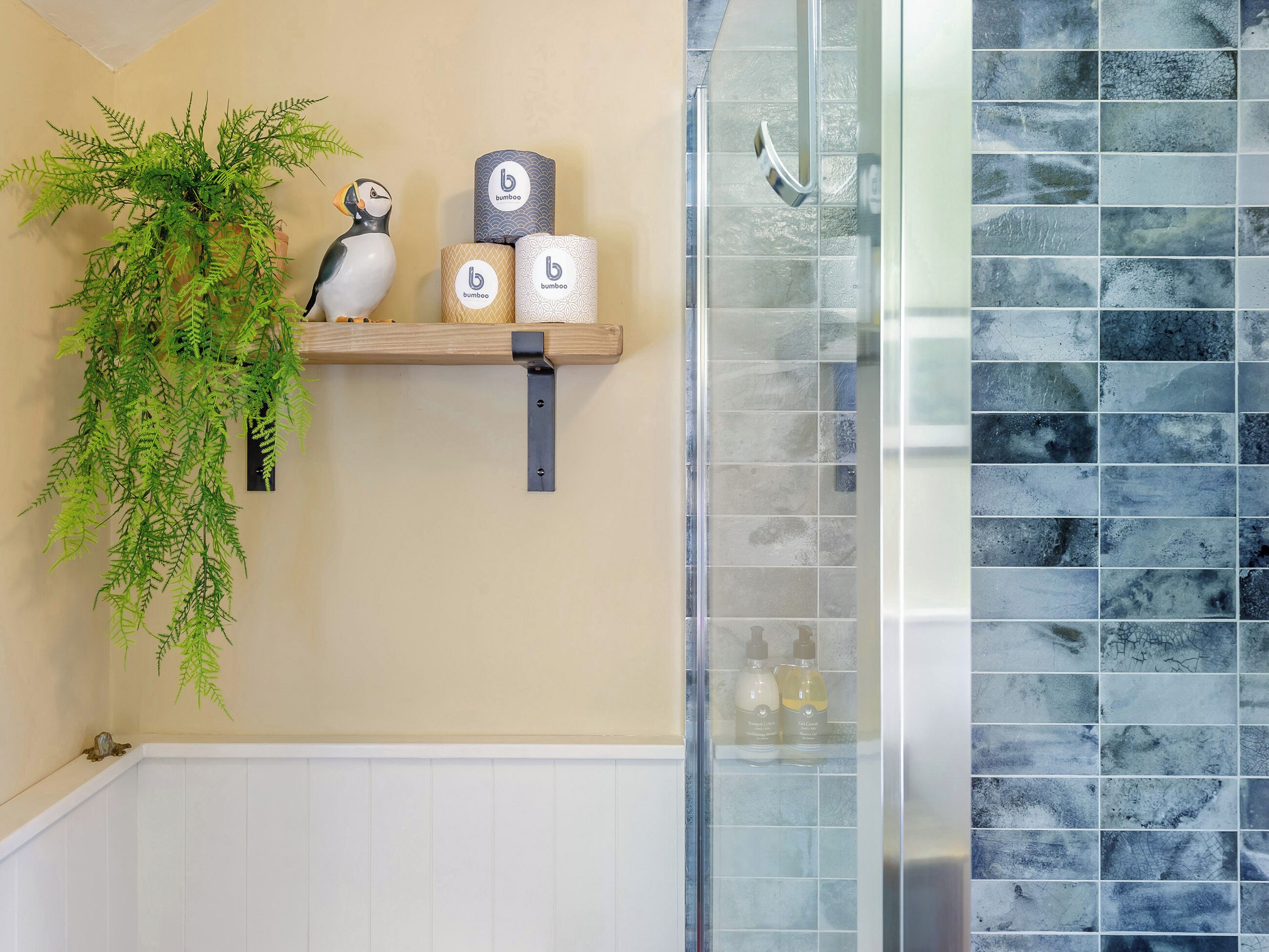 A bathroom with a shower, a shelf with a potted plant, and two bottles.