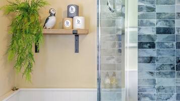 A bathroom with a shower, a shelf with a potted plant, and two bottles.