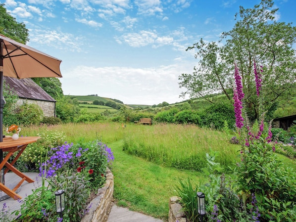 A garden with a wooden bench, a stone wall, and a stone building.