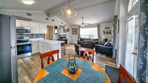 A modern kitchen with white cabinets and stainless steel appliances, a dining area with a round table and chairs, and a living room with a leather sofa and a ceiling fan. - 095 Gulf Loop - Beautiful Beach House with Golf Cart! (Panama City Beach)