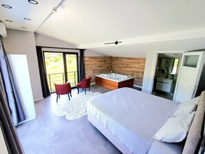 A modern bedroom with a large bed, a separate bathroom with a bathtub, and a seating area with two chairs.