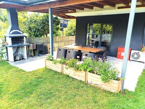 A covered outdoor patio with a grill, seating area, and planter boxes.