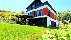 A modern two-story house with a large lawn and a covered patio area.