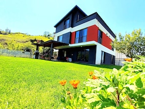 Una casa moderna de dos pisos con un amplio jardín y un patio cubierto.