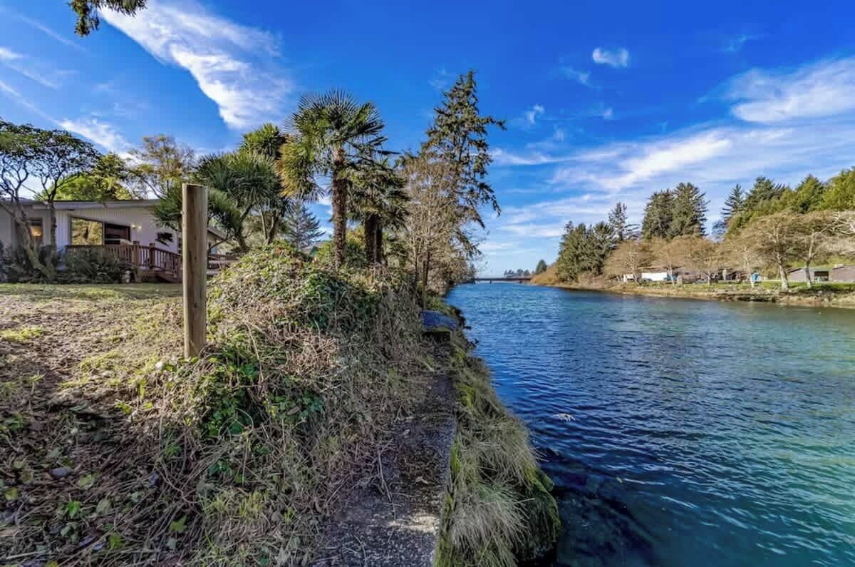 Una propiedad junto al río con una terraza de madera, un edificio pequeño y árboles frondosos.