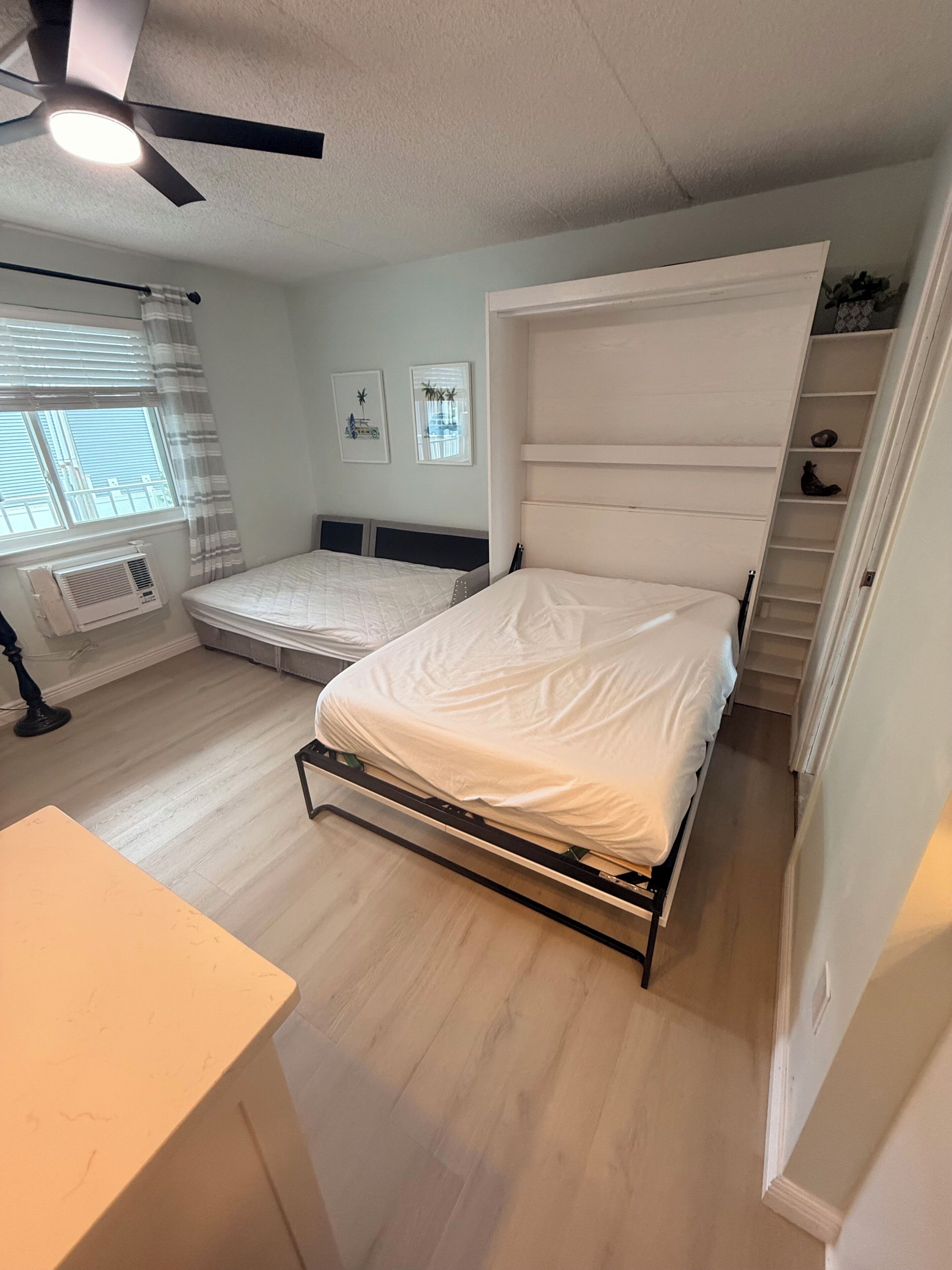 Een slaapkamer met een bed, een plafondventilator, een raam met zonwering en een radiator.
