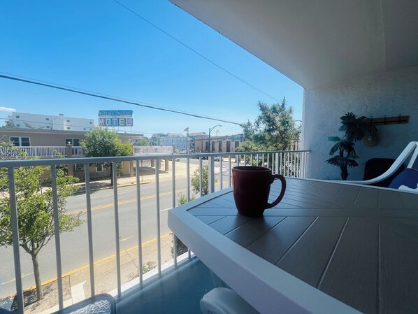 Un balcon avec une tasse rouge, une vue sur une rue bordée d’immeubles et une enseigne indiquant le « Sticking Sands Motel ».