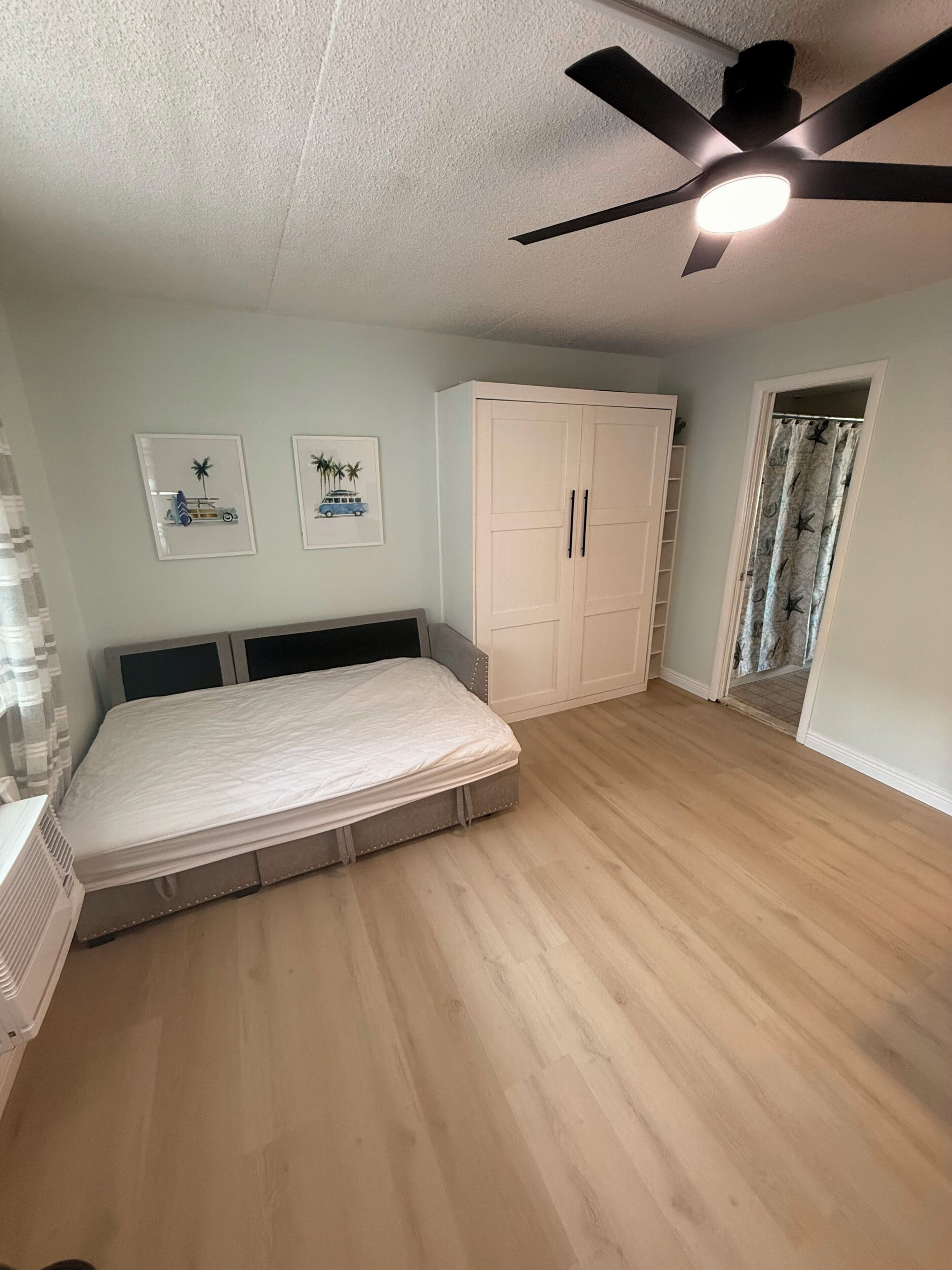 A bedroom with a bed, a ceiling fan, a wardrobe, and two framed pictures on the wall.