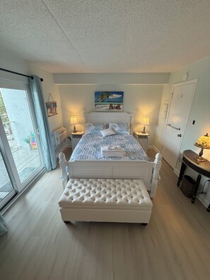 A bedroom with a bed, a bench, a painting, and a door.