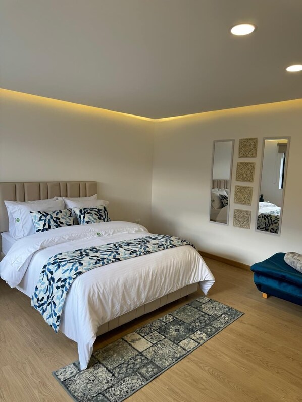A bedroom with a bed, a bedside table, a mirror, and a small seating area.