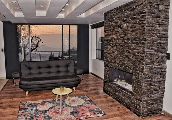 A modern living room with a black leather sofa, a small round table, and a large window with a view of the outdoors.