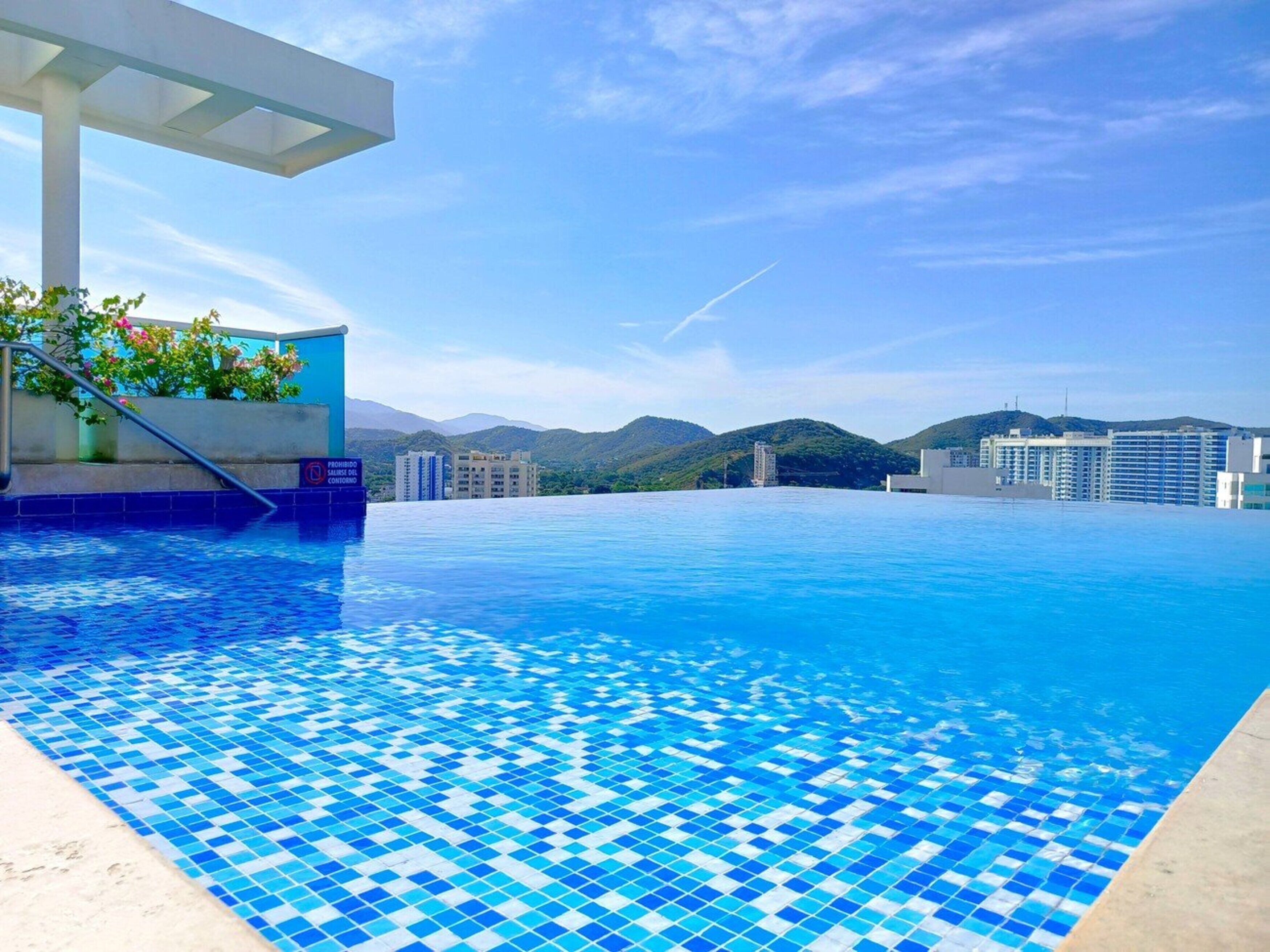 A rooftop infinity pool with a clear view of mountains and buildings in the background.